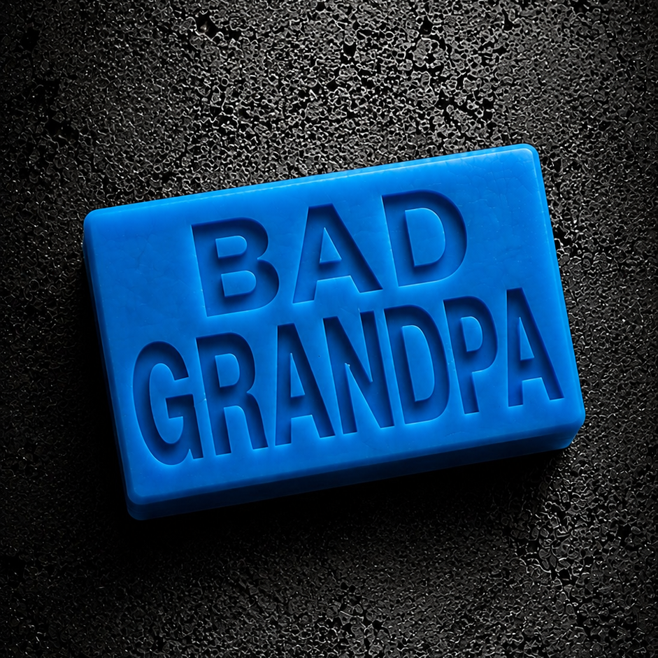 A bright blue rectangular bar of soap with the words 'BAD GRANDPA' embossed on the front, placed on a dark textured background.