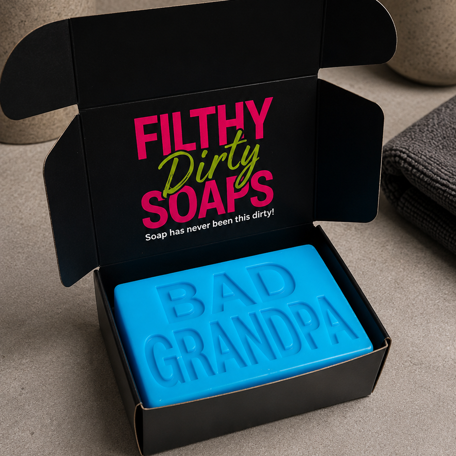 A bright blue bar soap embossed with 'BAD GRANDPA' sits in an open black gift box with the words 'FILTHY Dirty SOAPS' printed inside. 