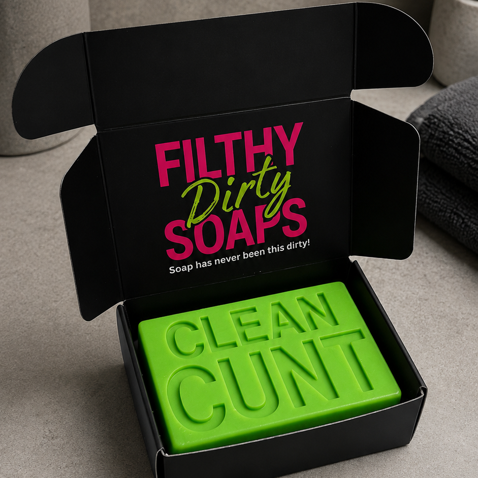 A bright green bar soap embossed with 'CLEAN CUNT' sits inside an open black gift box. The inside lid of the box features the text 'FILTHY Dirty SOAPS' in pink and green.