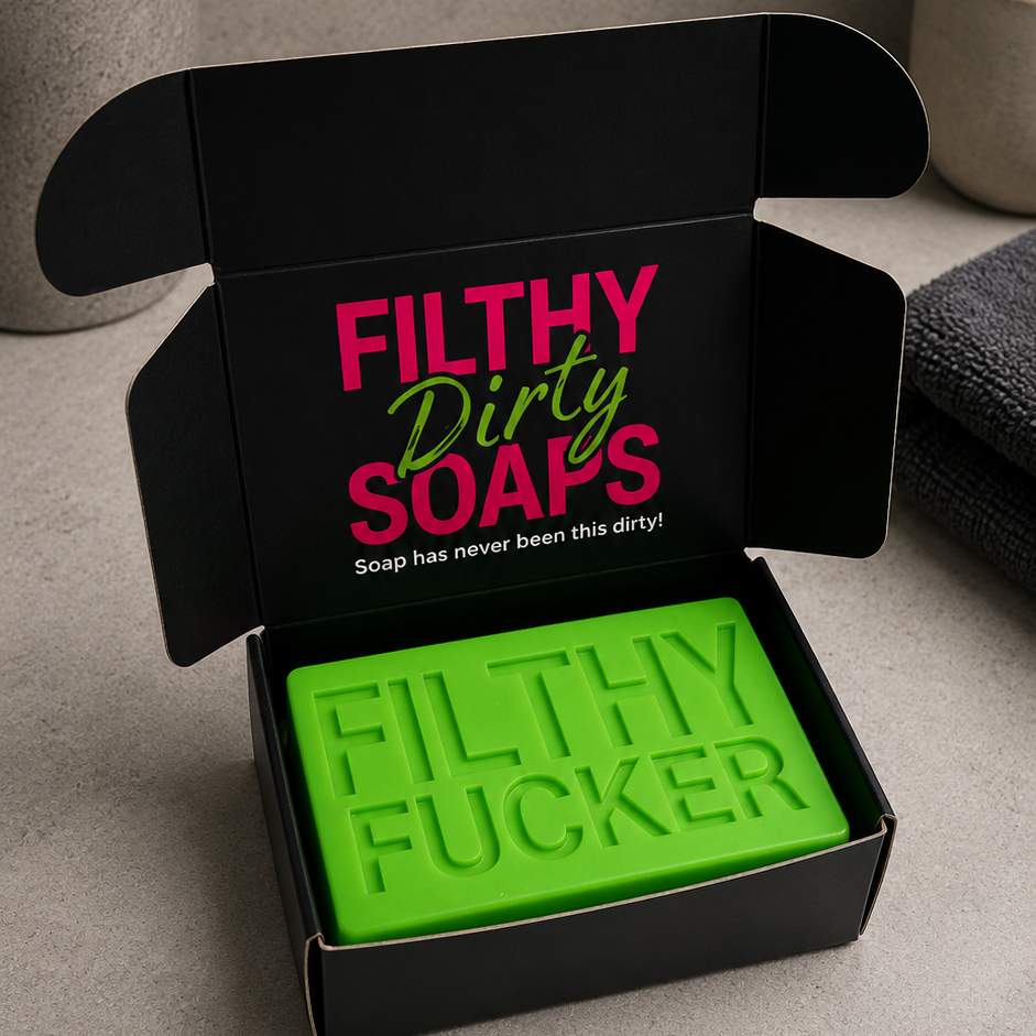 A bright green bar of soap embossed with the text 'FILTHY FUCKER' sits inside an open black gift box with the words 'FILTHY Dirty SOAPS' printed on the inside lid. 