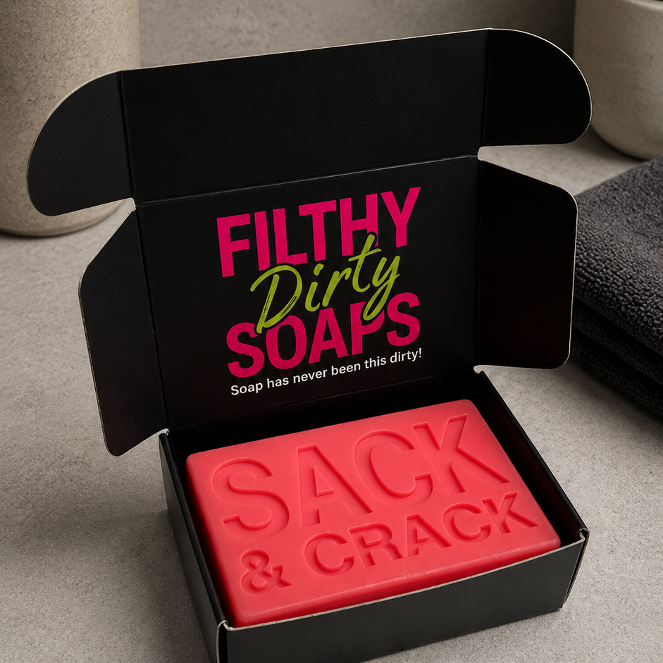 A red bar soap labeled 'SACK & CRACK' sits inside an open black gift box with the brand name 'FILTHY Dirty SOAPS' printed on the inside lid.
