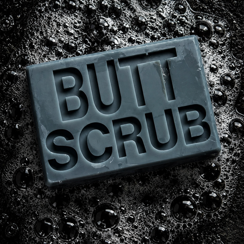 A rectangular dark gray butt scrub bar embossed with the words 'BUTT SCRUB' in large letters, resting on a wet, bubbly black surface.