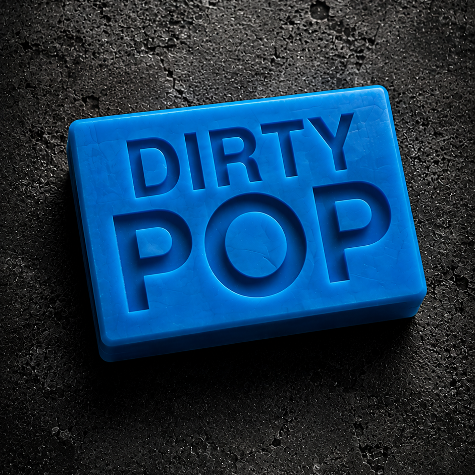 A bright blue rectangular bar of soap embossed with the words 'DIRTY POP' in raised lettering, photographed on a dark textured surface.