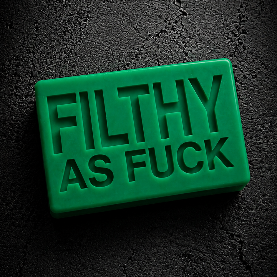 A bright green rectangular novelty item with the words 'FILTHY AS FUCK' embossed in large letters, photographed on a dark textured background.