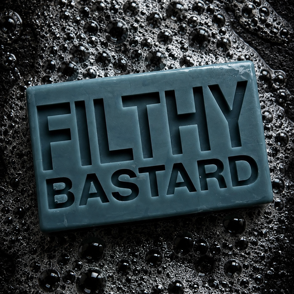 A rectangular bar of soap with the words 'FILTHY BASTARD' embossed on the front, resting on a dark, bubbly, water-dropped surface.